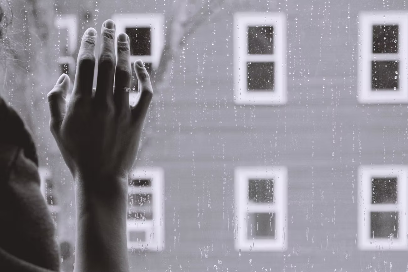 Hand an einer regennassen Fensterscheibe